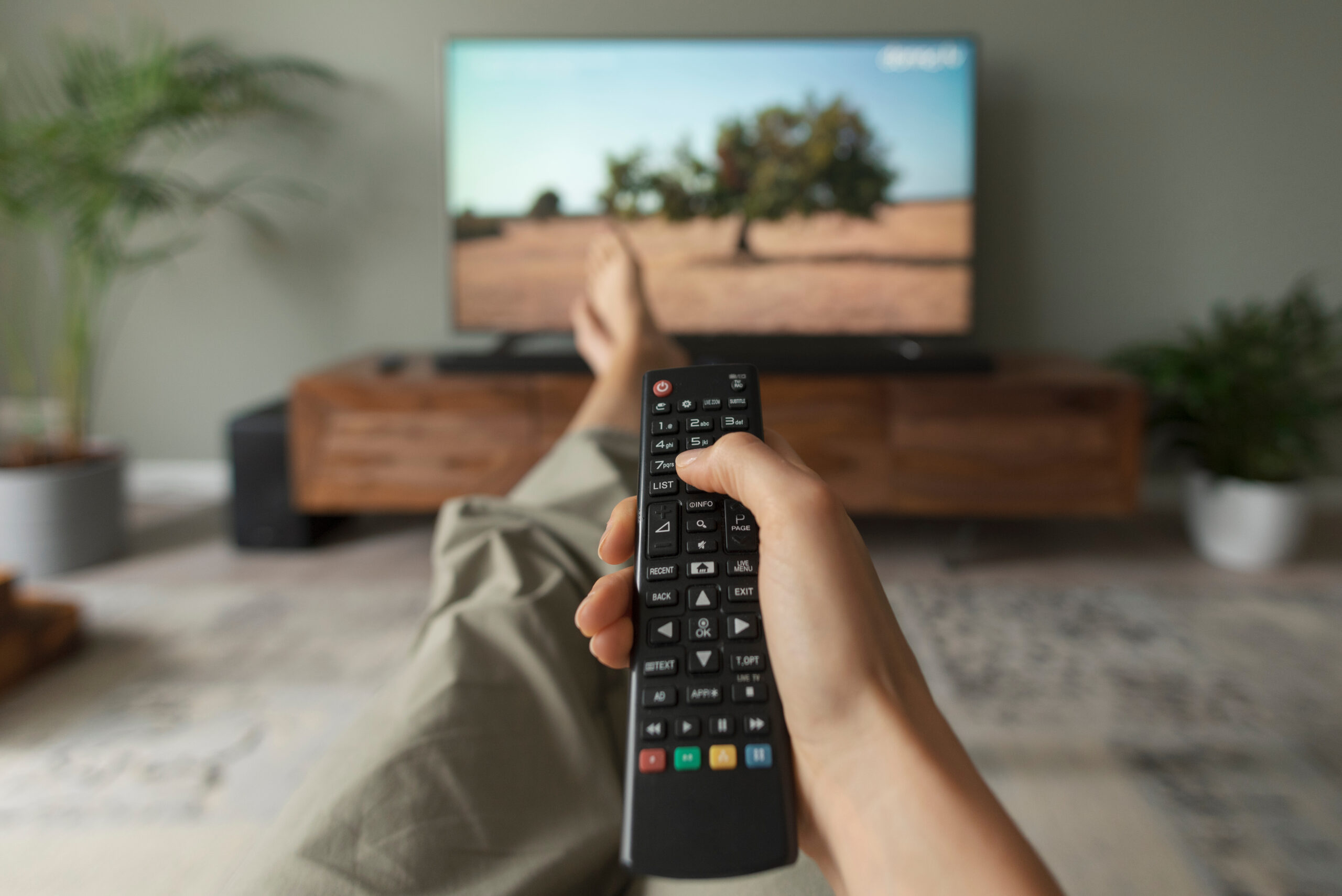 Woman watching TV at home and holding the remote control.