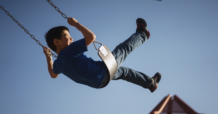 little boy swinging on swingset with blue sky behind him