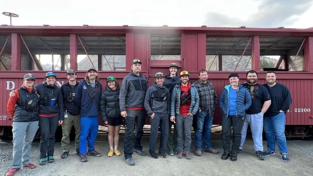 A rescue team of 13 stands near a red train car.