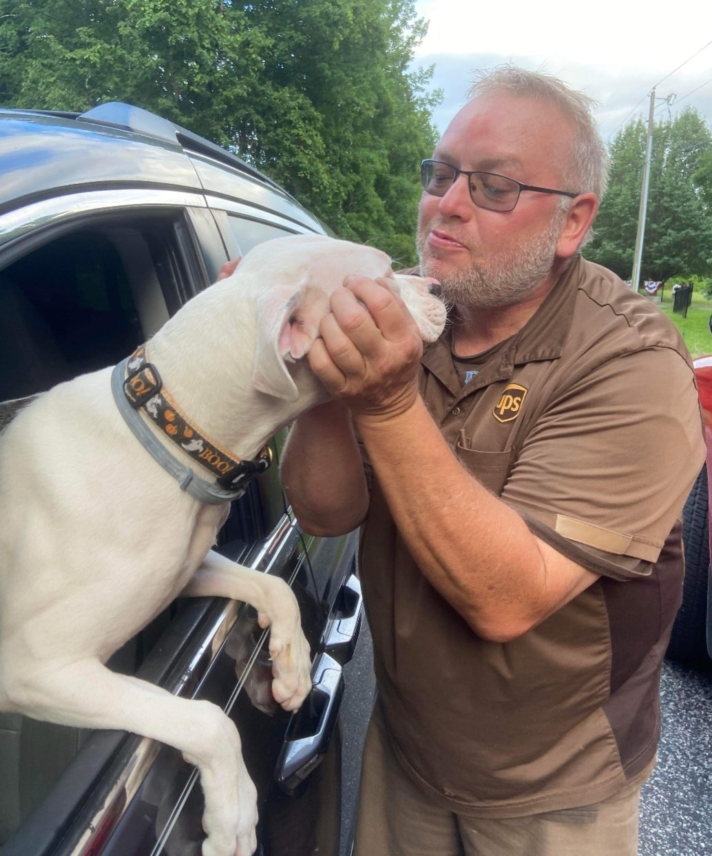 UPS man gives kisses to dog who is sticking his head out car window