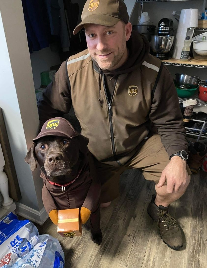 UPS man poses with brown dog dressed in a matching UPS outfit