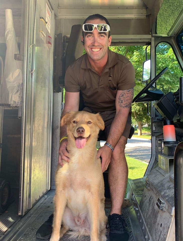 UPS man smiles with golden retriever in truck