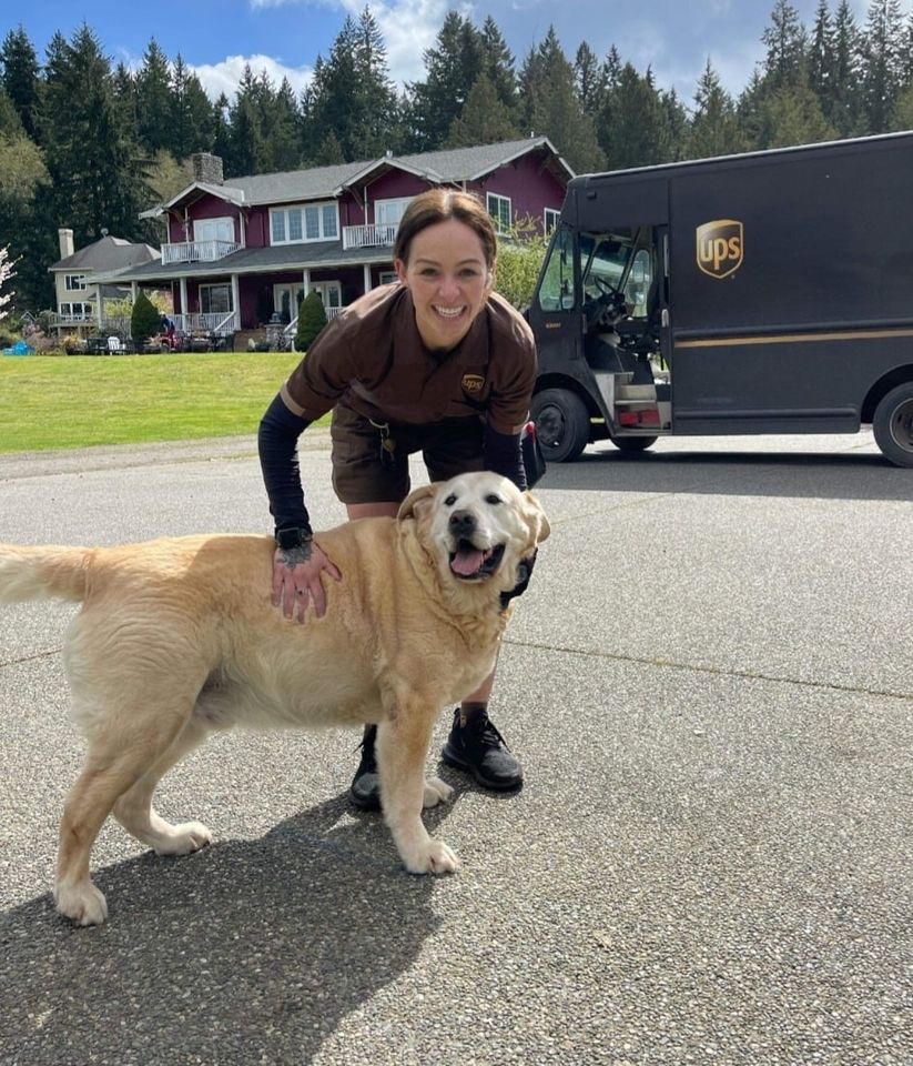 female UPS driver smiles while petting smiling dog