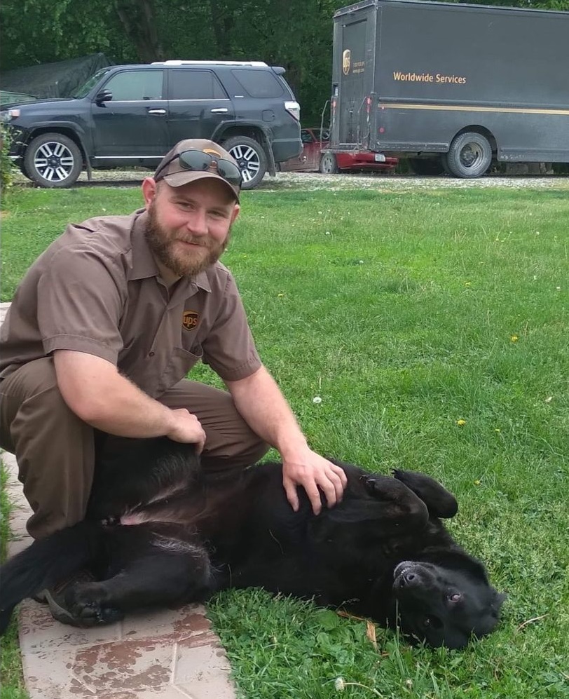 Smiling UPS man giving belly rubs to black dog on ground