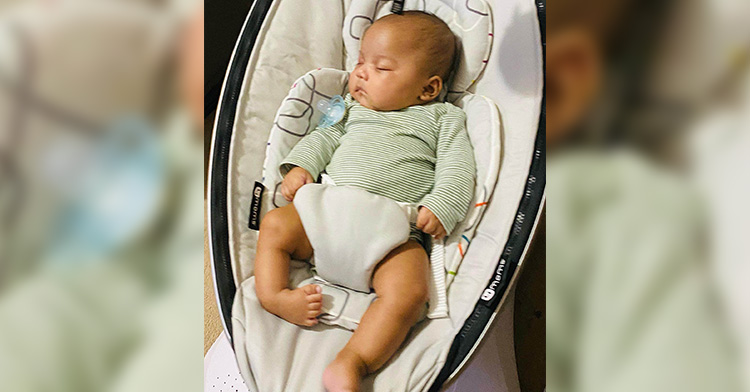 Dakari Miranda as an infant sleeping in a carrier. His right leg does not have a tibia bone and appears floppy and turned inward.