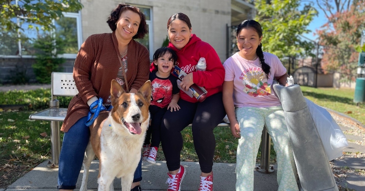 Virginia family of one adult and three children smiling as they sit on a bench outside with their dog, Dante, alongside them.