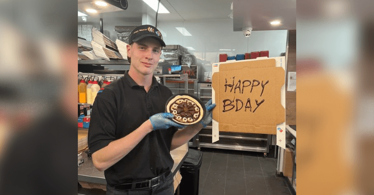 Domino's employee Miles holding a custom-made chocolate dessert pizza topped with churros & brownies.