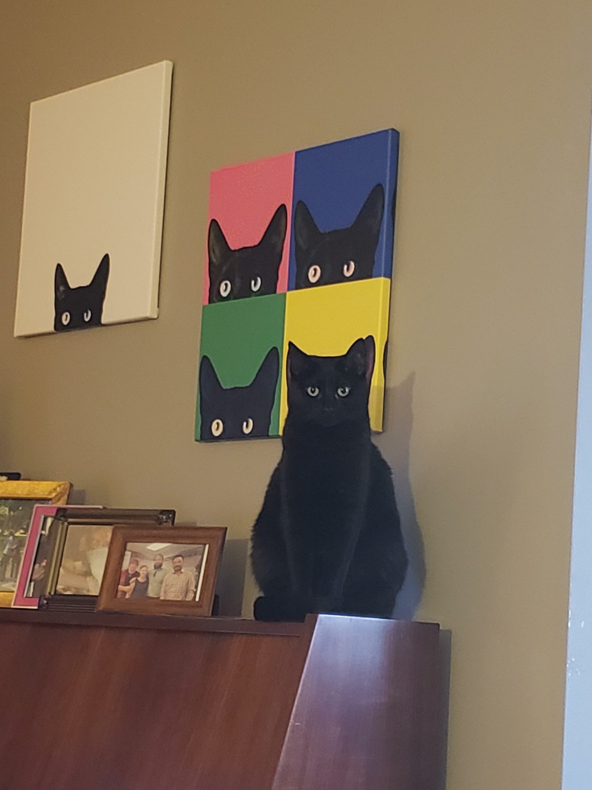 black cat sitting in front of artwork featuring a black cat