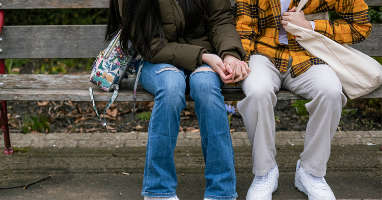 shot of two teens from the shoulder down sitting next to each other and holding hands