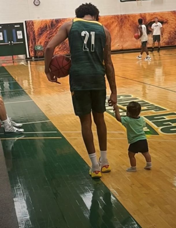 A basketball player holding a toddler's hand on a basketball court.