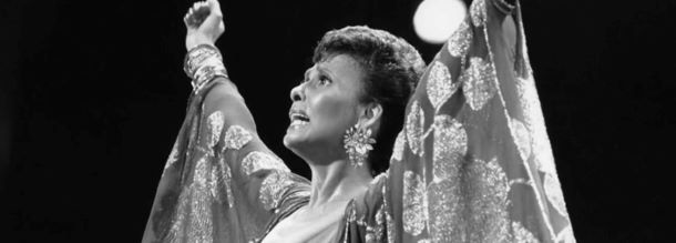Singer and actress Lena Horne raising her arms in the air as she looks out into the crowd.