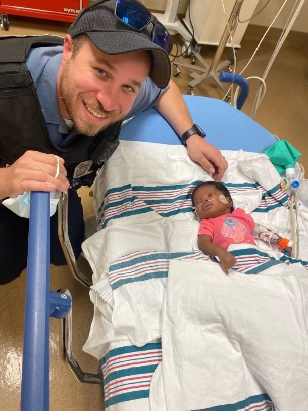 Police officer standing near baby in a hospital bed.