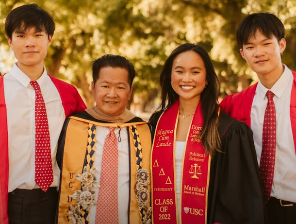 Four graduates, a father and his three children stand in their academic gowns.