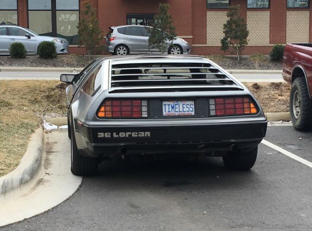 A car with a license plate that is timeless in all aspects. It is on a car that looks like the DeLorean and has a DeLorean bumper sticker.