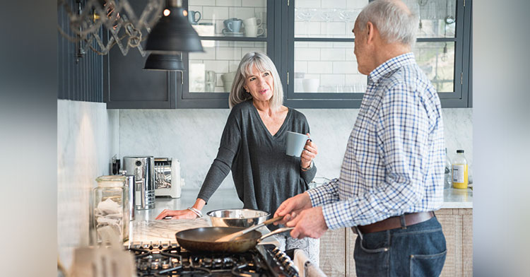 older couple talking in the kitchen while the man cooks