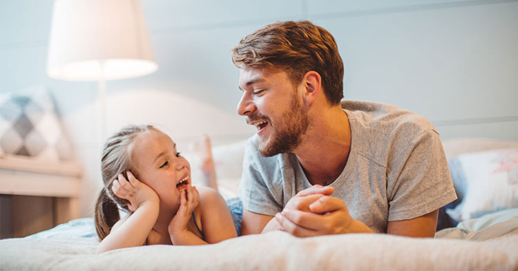 father and daughter lying stomach down on bed and smiling at each other