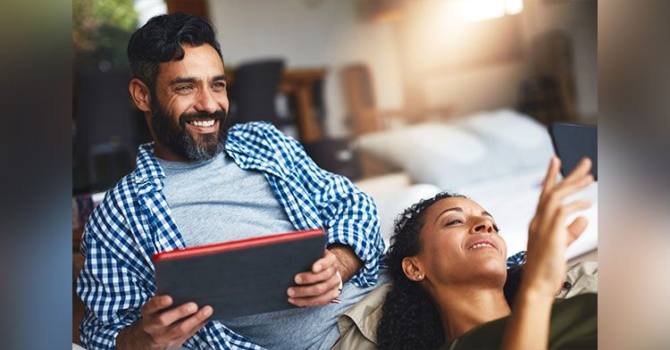 man and woman sitting close to each other and smiling while holding a phone and tablet