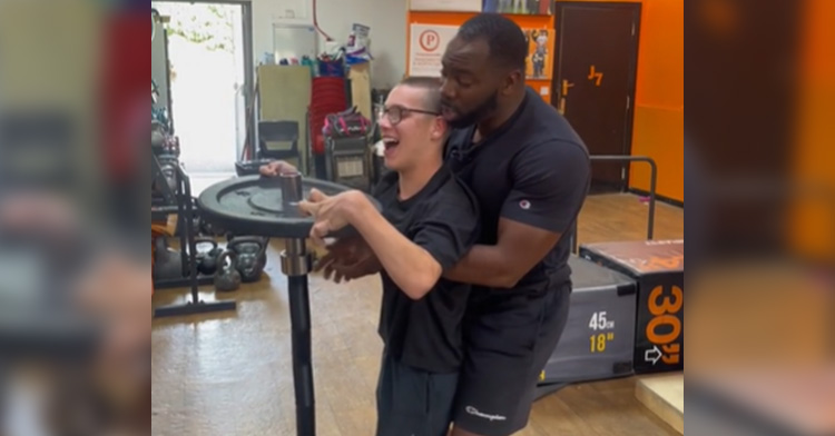 Jason McLean helping a young man lift a weight.