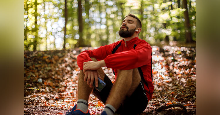 man sitting down in forest and closing his eyes