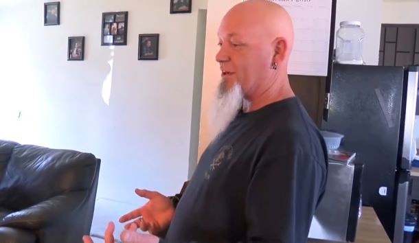 A man is standing in his home speaking about his pet squirrel.