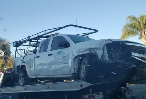 A white truck with front-end damage is on a tow truck.