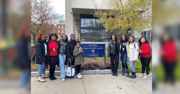 A group of African-American female scientists stand near a sign on Yale University's campus, including Bobbi.