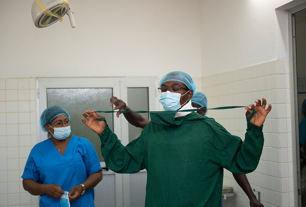 Dr. Grégoire Akakpo-Numado being assisted while putting on scrubs before cleft surgery.
