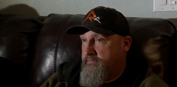 A man wearing a hat with a gray beard is sitting on a couch.