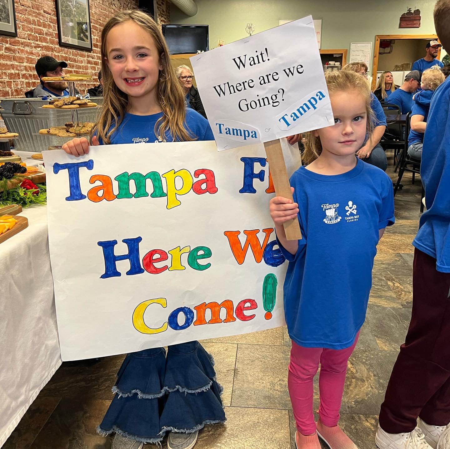 two little girls holding up signs that say "Tampa FL here we come" and "wait! Where are we going? Tampa"