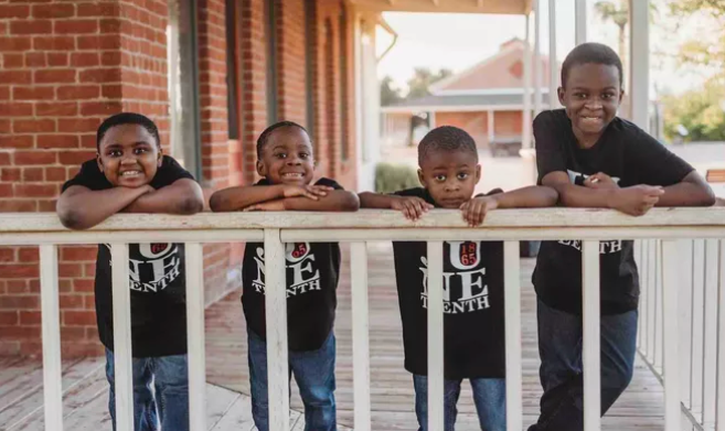 Kayla Howard's four sons smiling and leaning on a porch railing. 
