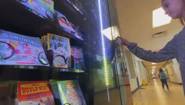A student is getting a book from a vending machine.