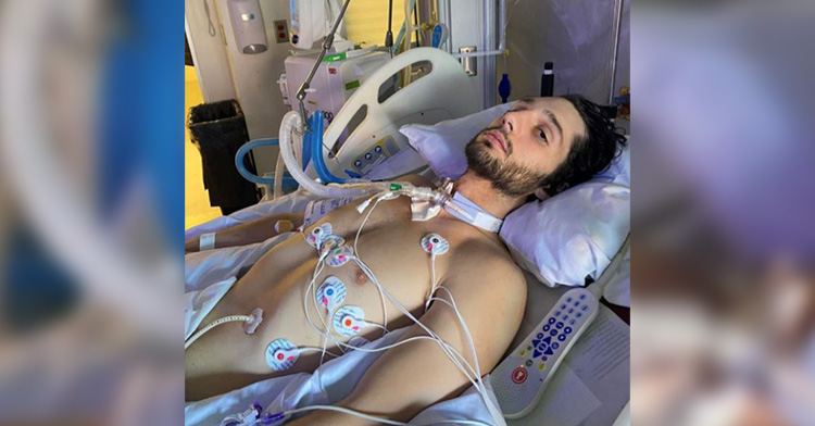 Cody lays in a hospital bed with machines and tubes hooked to him. He looks uncomfortable as he stares into the camera.