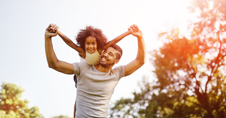 dad carrying daughter on his back in the park