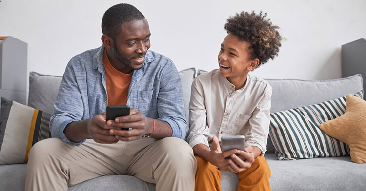 father and son sitting together on couch and smiling at each other