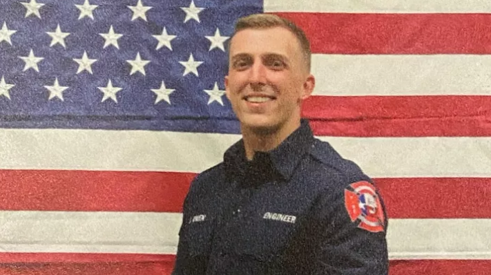 Firefighter Jake Owen smiling in front of an American flag