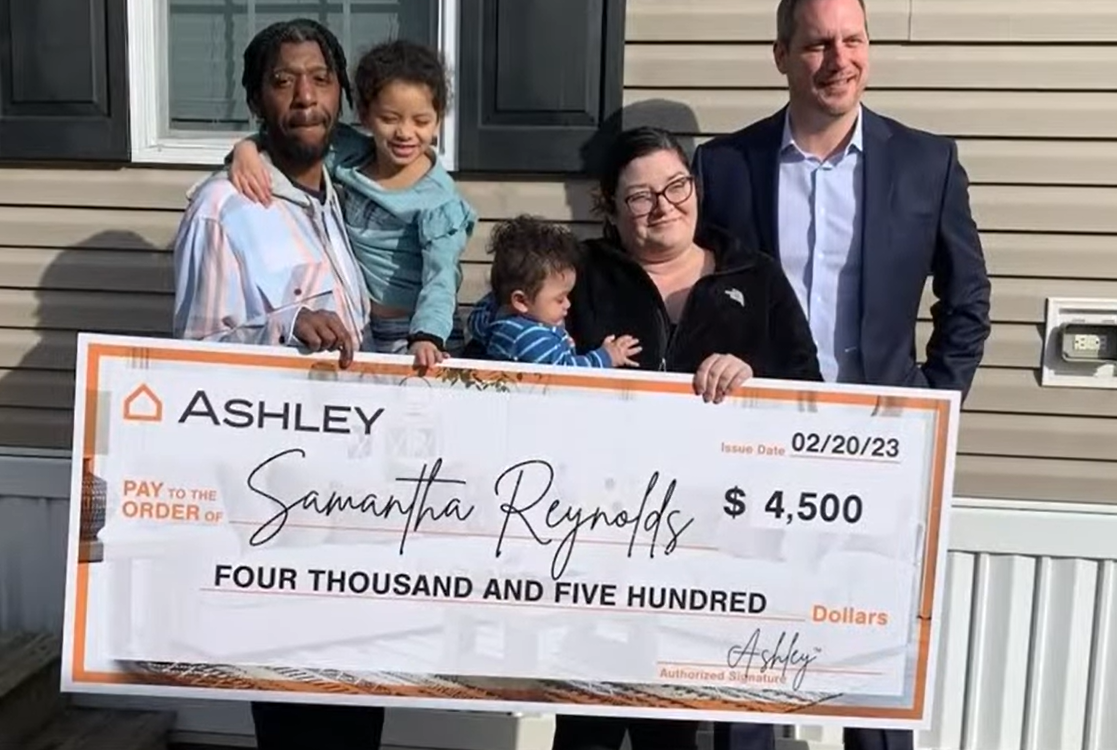 Simmons-Russell family with Ashley rep, holding big check from Ashley HomeStores.