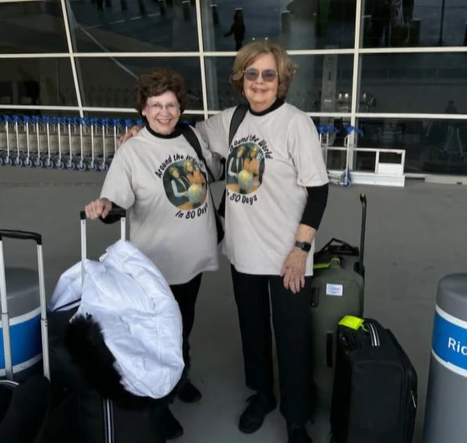 Sandy Hazelip and Ellie Hamby at the airport wearing matching "Around the world at 80" tee shirts.