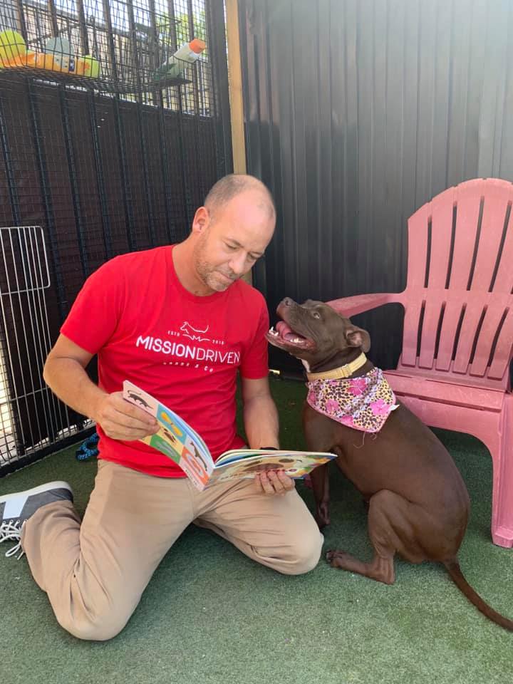 Scott Poore reading to Queen the dog as she wears a bandana