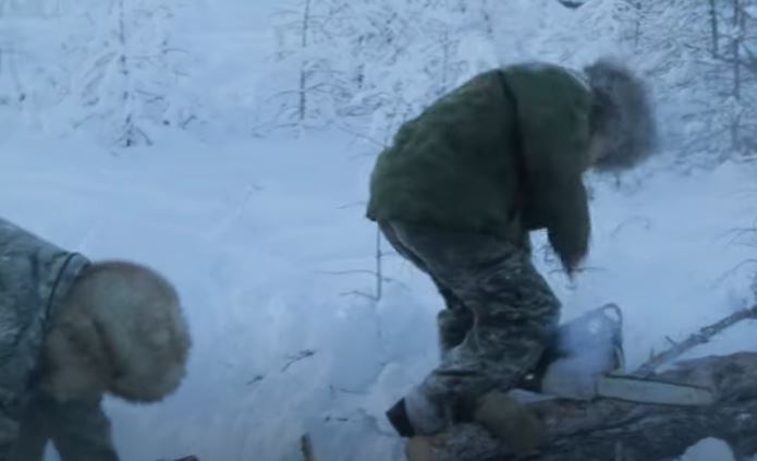 Two bundled-up men cutting wood for fires with a chainsaw.