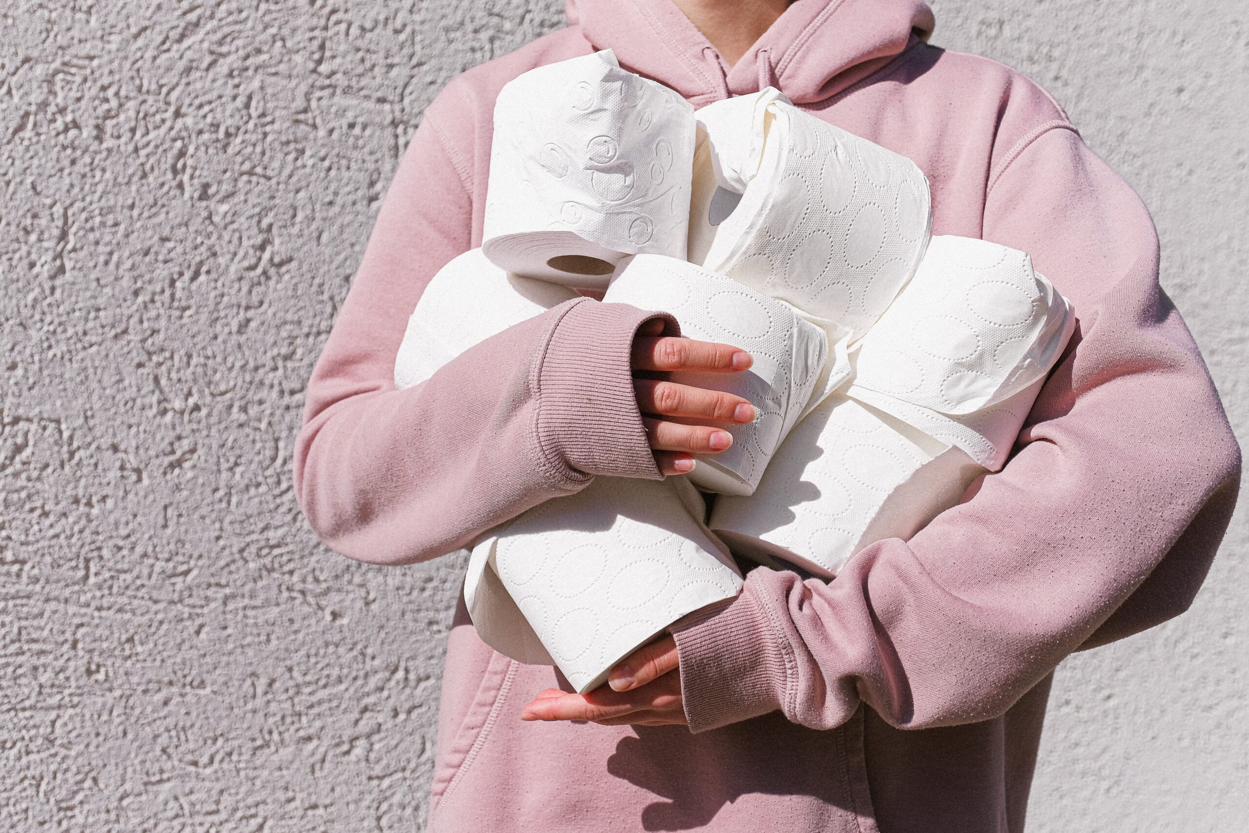 person in pink hoodie holding armful of toilet paper