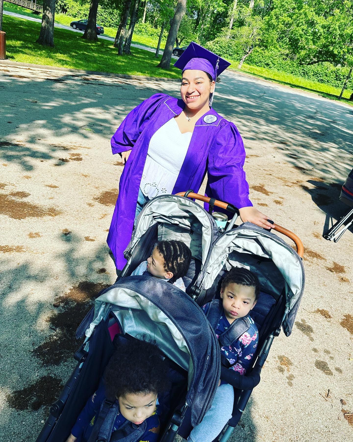 Shariya Smalls in graduation cap and gown pushing triplets in stroller.