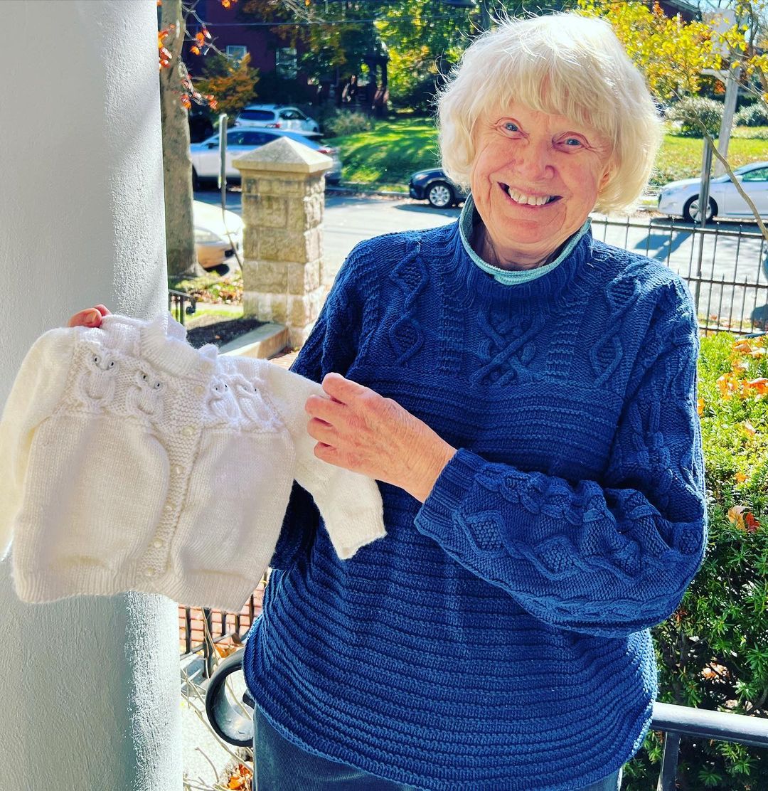 woman holds up baby sweater she finished for Loose Ends project.