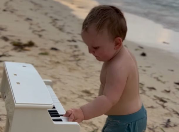 Baby Gavriil Scherbenko plays a toy keyboard on the beach.