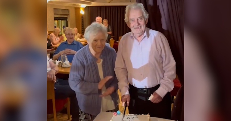 Peter McKenna smiles as he starts to cut his 62nd wedding anniversary cake. Pauline McKenna stand next to him and claps.