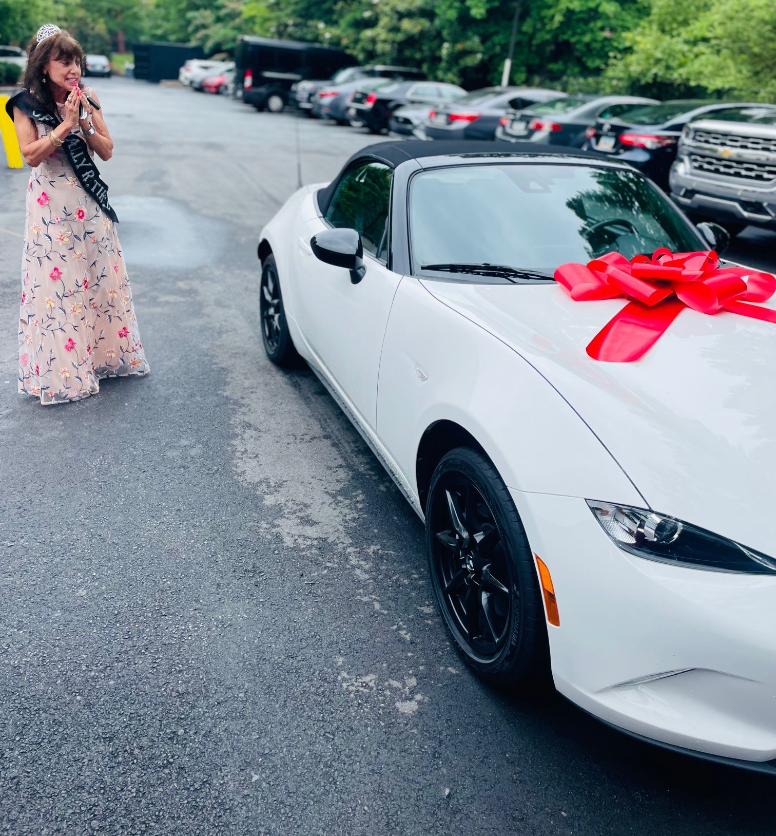 Lynne Gomez hold her hands close to her face as she reacts to the white Mazda Miata her boss, Ray, is gifting her.