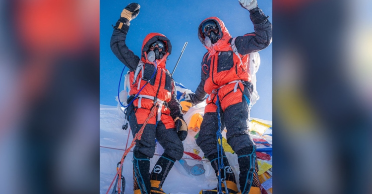 Scott and Shayna raise their arms in the air in celebration on the summit of Mount Everest.