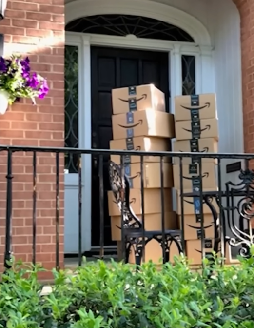 Two large stacks of Amazon packages sit outside a front door.