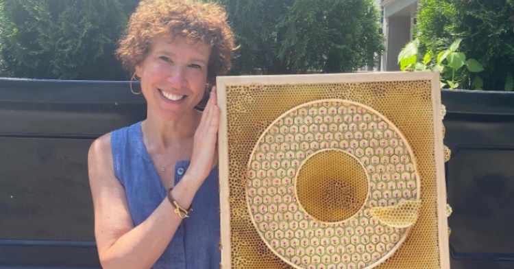 Artist Ava Roth smiles as she holds up one of her art pieces that she made with the help of local honeybees.