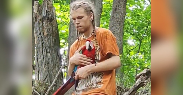 A man holds Guru the bird in his arms as he walks through a forest.