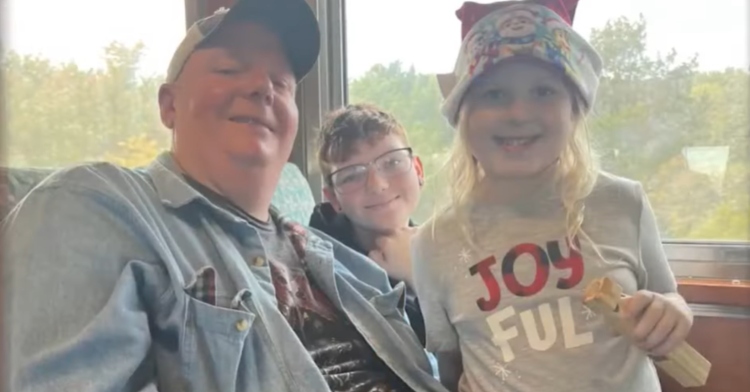 Chris Meffen smiles and poses with two young children on a train.